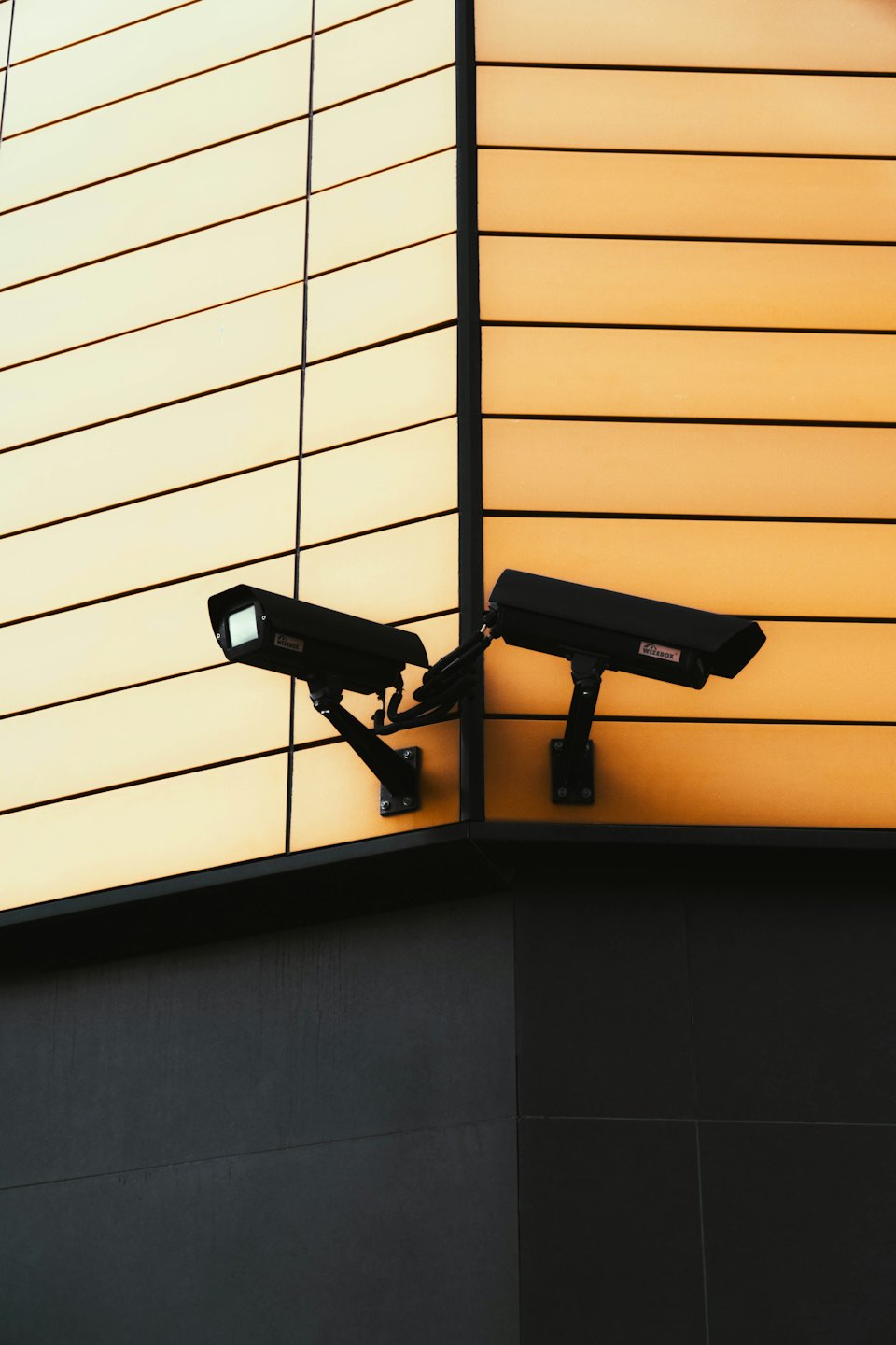 Two black security cameras on a building's exterior corner.